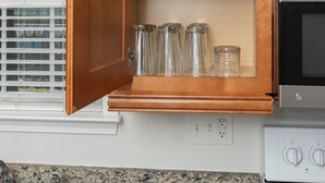 A kitchen with wooden cabinets, a granite countertop, a stove, and a window with blinds.