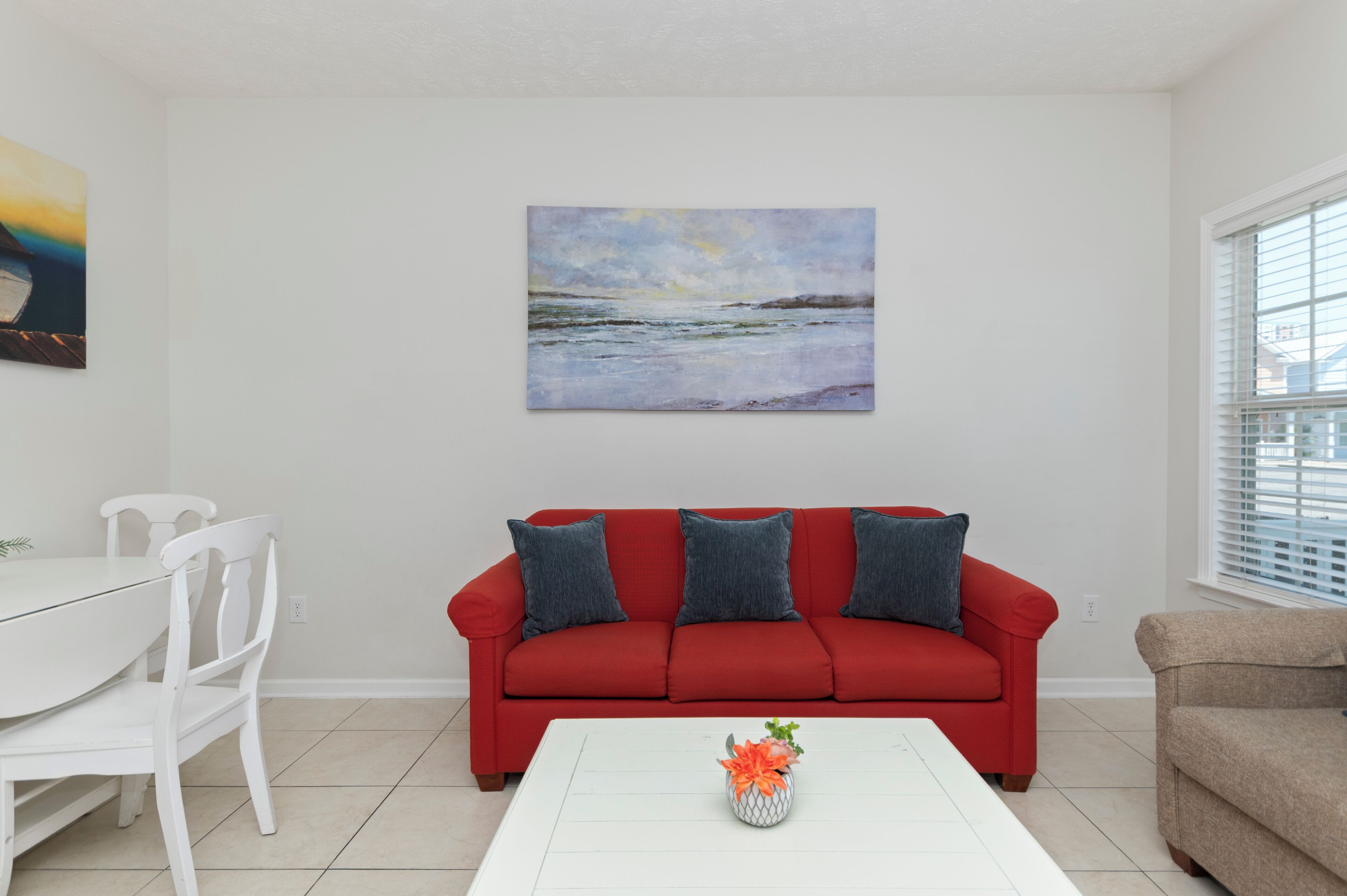 Un salon avec un canapé rouge, une table basse blanche et un tableau accroché au mur.
