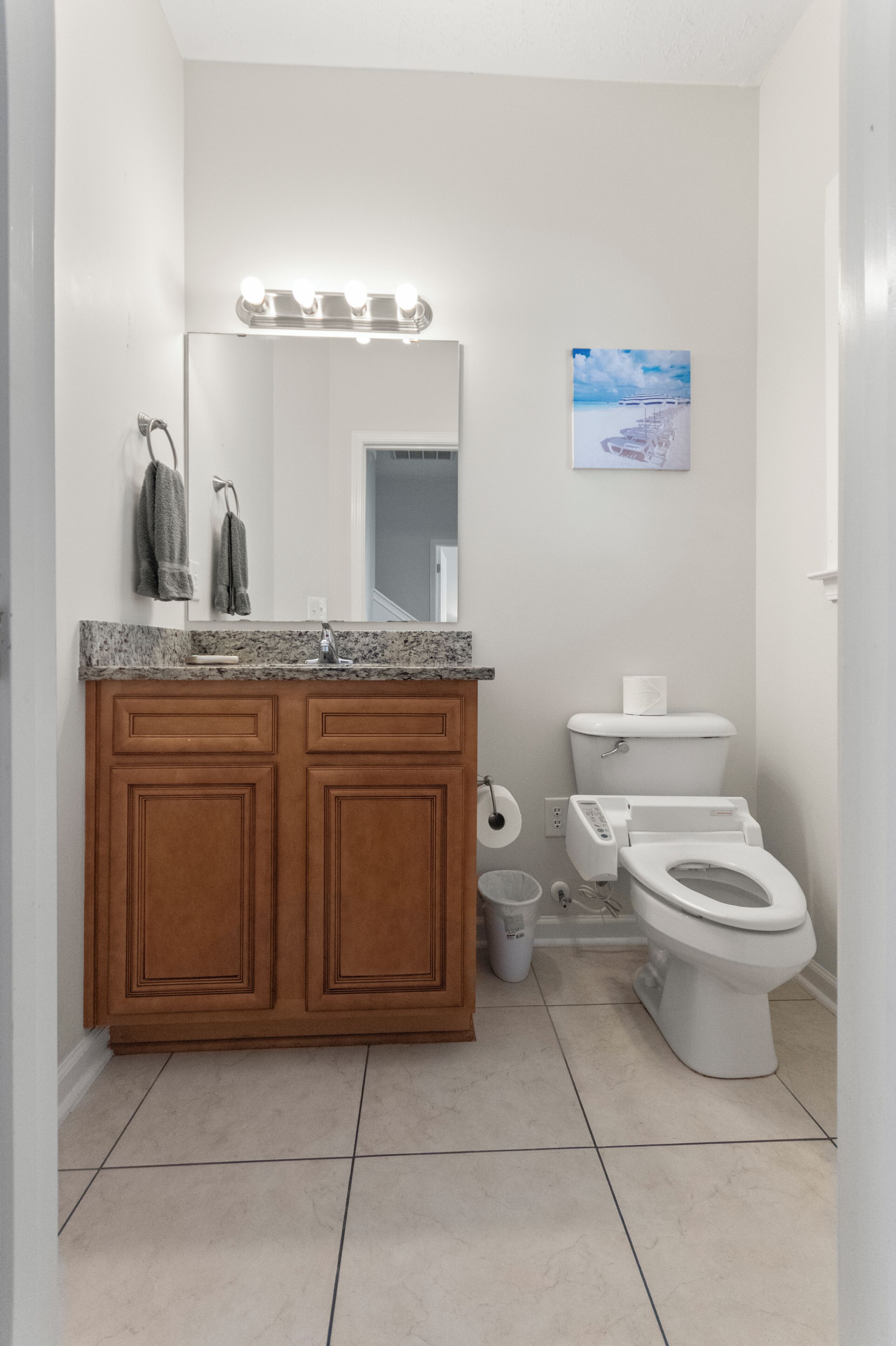 Une salle de bain avec un meuble-lavabo en bois, un miroir avec éclairage intégré, des toilettes et une poubelle.
