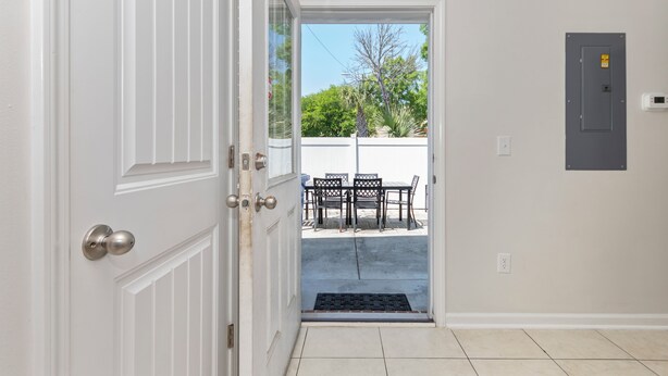 An open door leading to an outdoor patio with a table and chairs, a power outlet, and a wall-mounted electrical box.