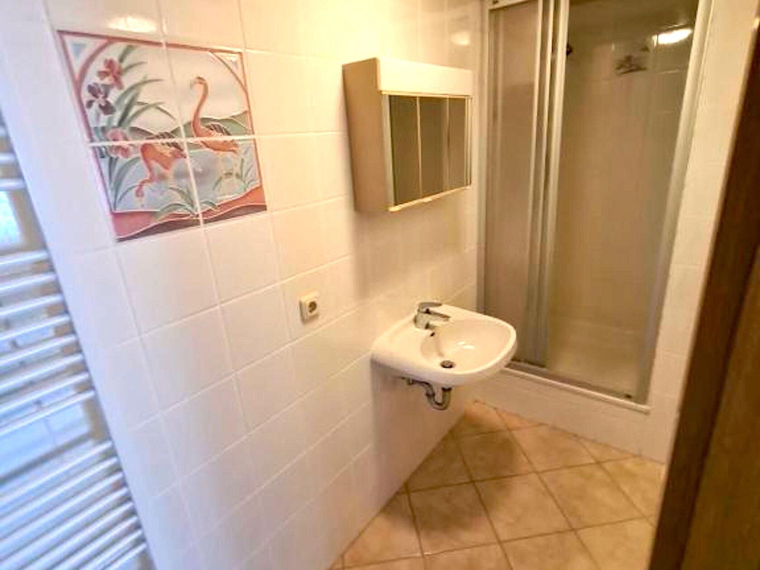 A bathroom with white tiles, a sink, a mirror, and a shower.