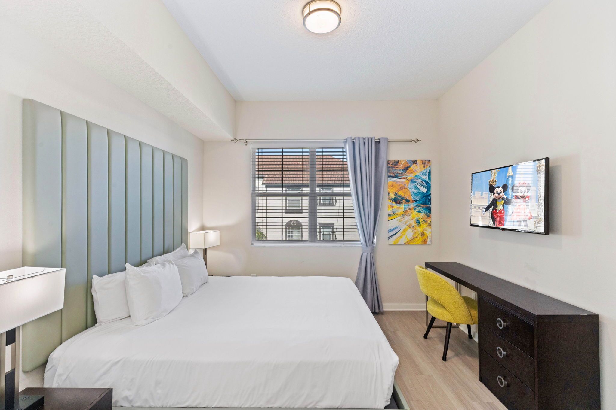 Une chambre d’hôtel moderne équipée d’un grand lit, d’un bureau, d’une chaise, d’une télévision et d’une fenêtre avec des rideaux.