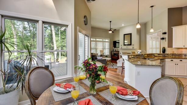 A dining area with a wooden table set for four, surrounded by chairs. There is a vase with flowers and a fruit bowl on the table. - Hilton Head Island Resort Home w/ Fire Pit! (Hilton Head Island)