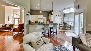 A spacious living area with hardwood flooring, a sofa with a 'FAITH' pillow, a patterned rug, and a dining area with a table and chairs. - Hilton Head Island Resort Home w/ Fire Pit! (Hilton Head Island)