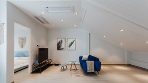 Une chambre de style loft moderne, avec un plafond en pente, un grand lit, une télévision et un canapé bleu.