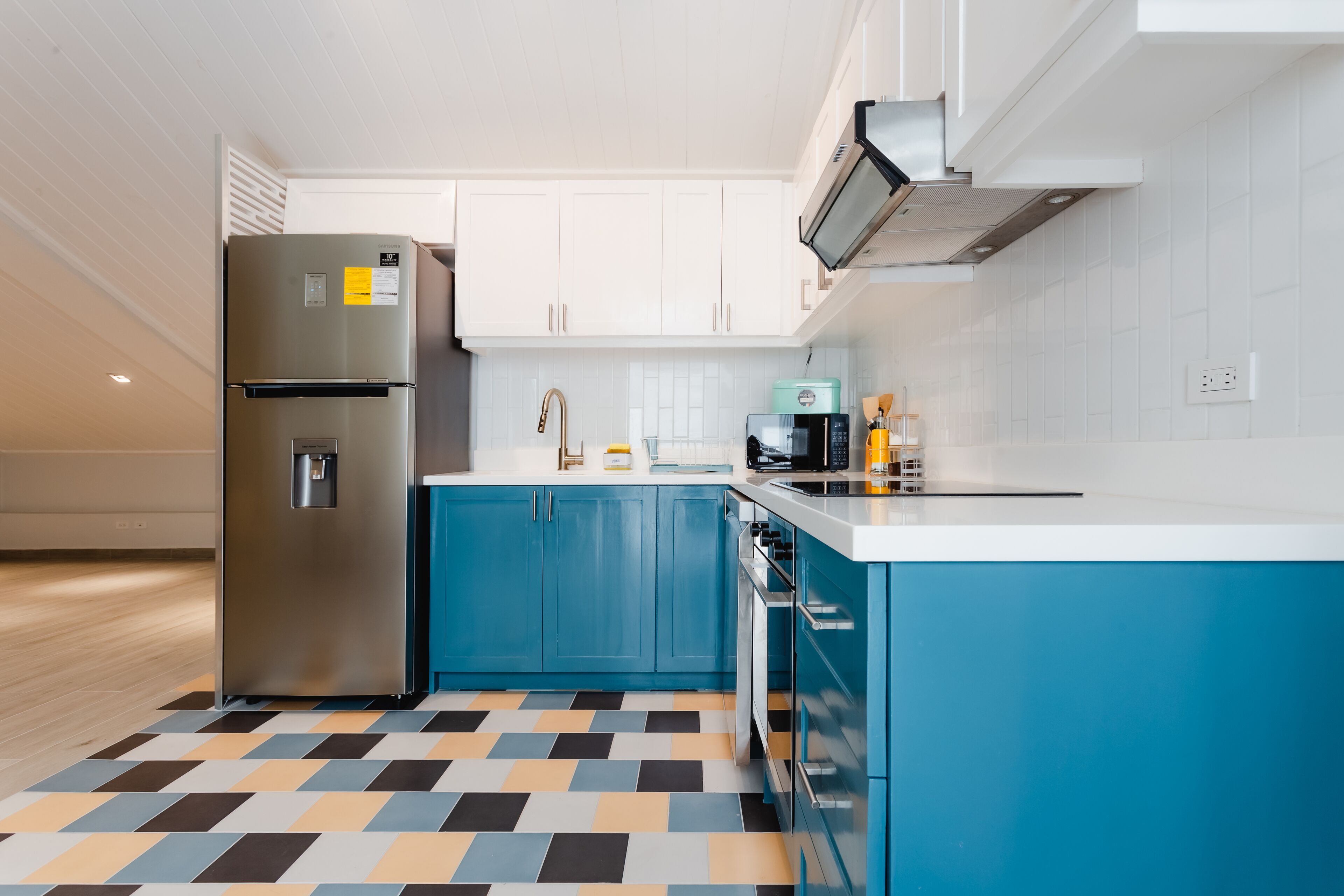 A modern kitchen with a stainless steel refrigerator, blue cabinets, a white countertop, and a patterned floor.