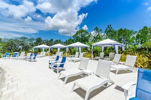 Relax by the serene pool surrounded by lush greenery and comfortable lounge chairs under canopies.