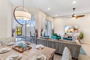 Relax in this inviting living area with a dining table, comfortable sofa, and TV, offering a view of the outdoor pool.