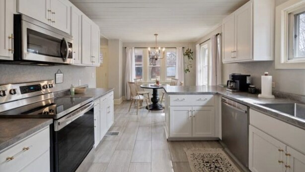 A modern kitchen with stainless steel appliances, white cabinetry, and a central island with chairs. - Cobblestone Cottage, 4 Bedroom, centrally located (La Crosse)