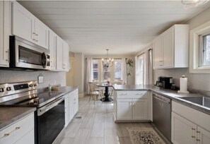 A modern kitchen with stainless steel appliances, white cabinetry, and a central island with chairs. - Cobblestone Cottage, 4 Bedroom, centrally located (La Crosse)