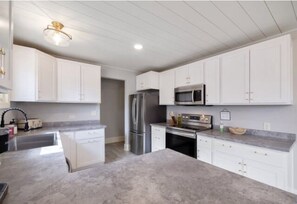 A modern kitchen with white cabinetry, stainless steel appliances, and a marble countertop.