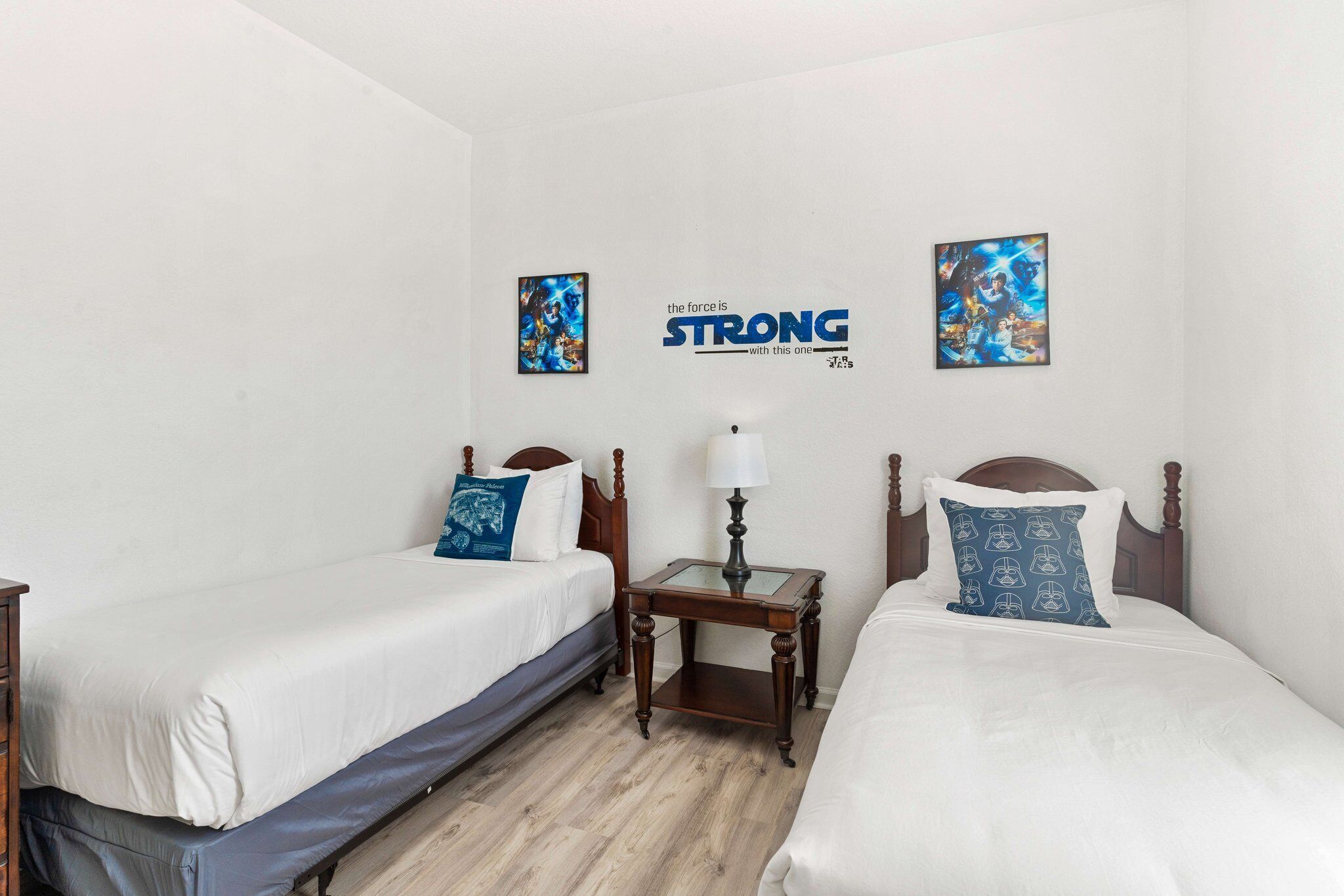 A hotel room with two single beds, a nightstand with a lamp, and two wall art pieces.
