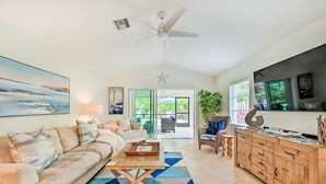 A spacious living room with a large sofa, a coffee table, and a dining area with wooden cabinets. - REYO de SOL, a remodeled tropical home with private heated pool, near beach! (Naples)