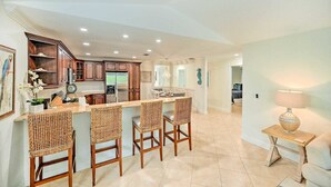 A spacious kitchen with a central island, wooden bar stools, and a dining area. - REYO de SOL, a remodeled tropical home with private heated pool, near beach! (Naples)