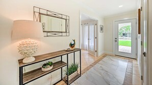 A hallway with a console table, a mirror, and a door leading to a garden. - REYO de SOL, a remodeled tropical home with private heated pool, near beach! (Naples)