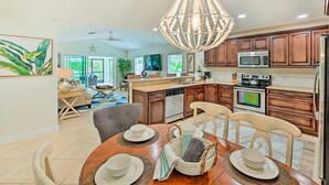 A modern kitchen with wooden cabinets, a stainless steel oven, and a microwave. There is a dining area with a table set for two. - REYO de SOL, a remodeled tropical home with private heated pool, near beach! (Naples)