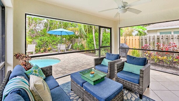 A covered patio with wicker furniture, a pool, and a view of a lush garden. - REYO de SOL, a remodeled tropical home with private heated pool, near beach! (Naples)