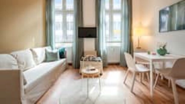 Moderni hotellihuone, jossa on sohva, ruokapöytä tuoleineen ja suuri ikkuna, jossa on verhot.