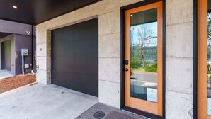 Ein moderner Gebäudeeingang mit Betonfassade, einer großen Garagentür und einer Glastür mit Holzrahmen.
