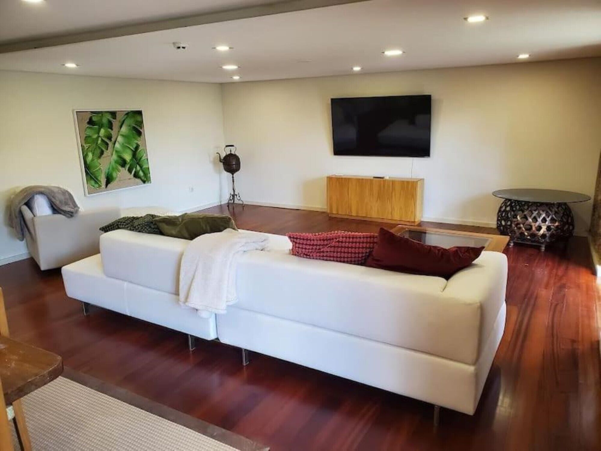 Un salon moderne avec un canapé blanc, un meuble en bois, un téléviseur à écran plat et une plante décorative.
