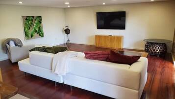 Un salon moderne avec un canapé blanc, un meuble en bois, un téléviseur à écran plat et une plante décorative.