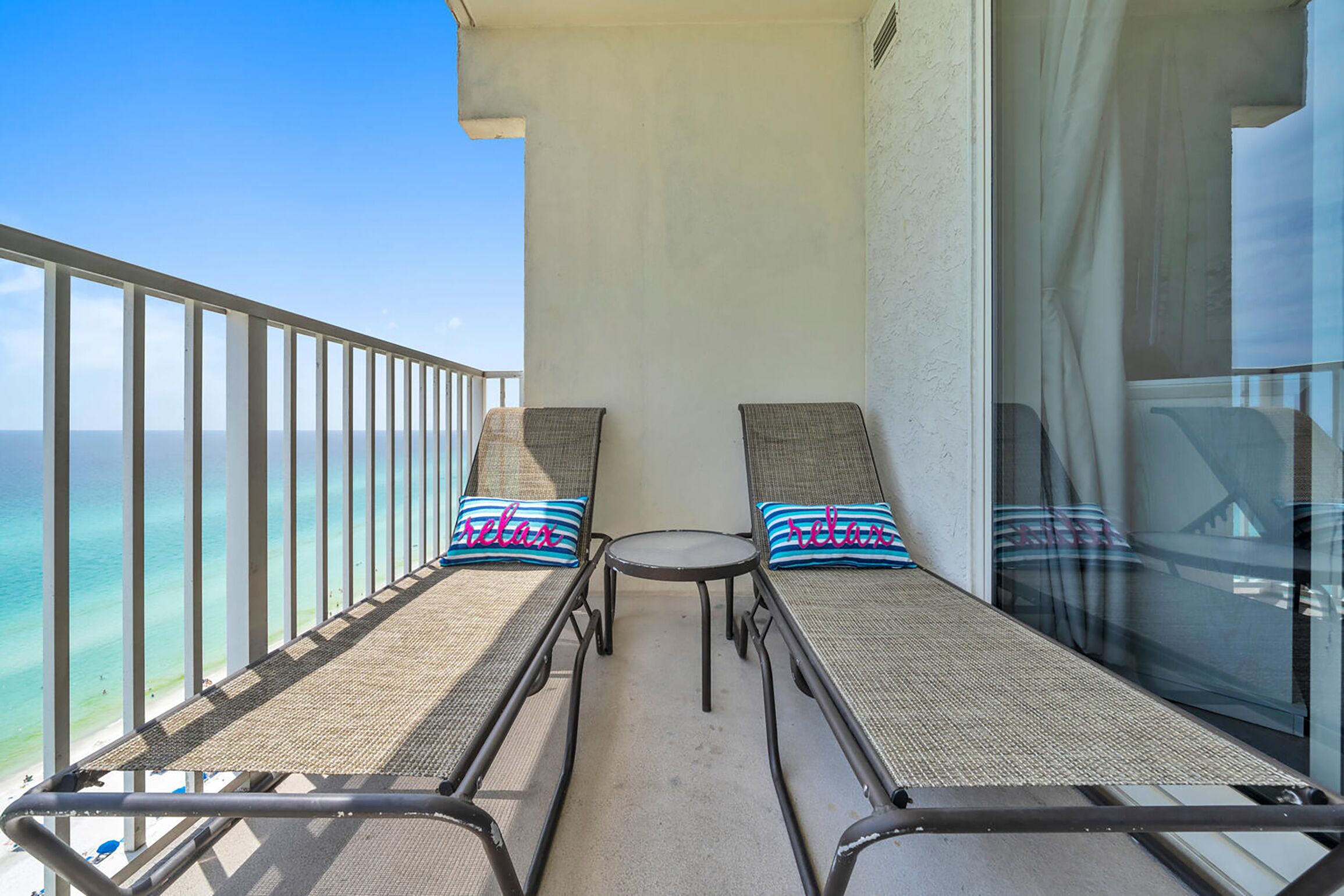 Ein Balkon mit zwei Liegestühlen, jeweils mit Kissen, mit Blick auf einen Strand.