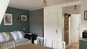 Una stanza con un tavolo da pranzo, sedie, un letto con cuscini decorati, una porta bianca e una parete con quadri.