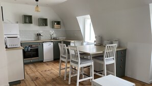 Una cucina moderna con mobili bianchi, pavimento in legno e zona pranzo con sedie bianche.