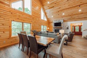 Cozy cabin with a high ceiling, exposed beams, and a stone fireplace, offering a comfortable seating area and a flat-screen TV.