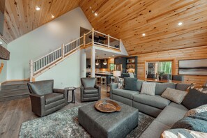 Relax in this spacious living area with a high ceiling and modern staircase, featuring a sectional sofa, armchairs, and a flat-screen TV.