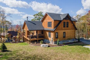 Enjoy outdoor activities and gatherings on the spacious deck of this cabin-style home, surrounded by a well-maintained lawn and trees.