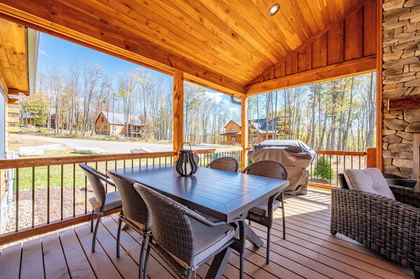 Relax on the covered deck, surrounded by nature, with a stone fireplace and comfortable seating for dining or socializing.