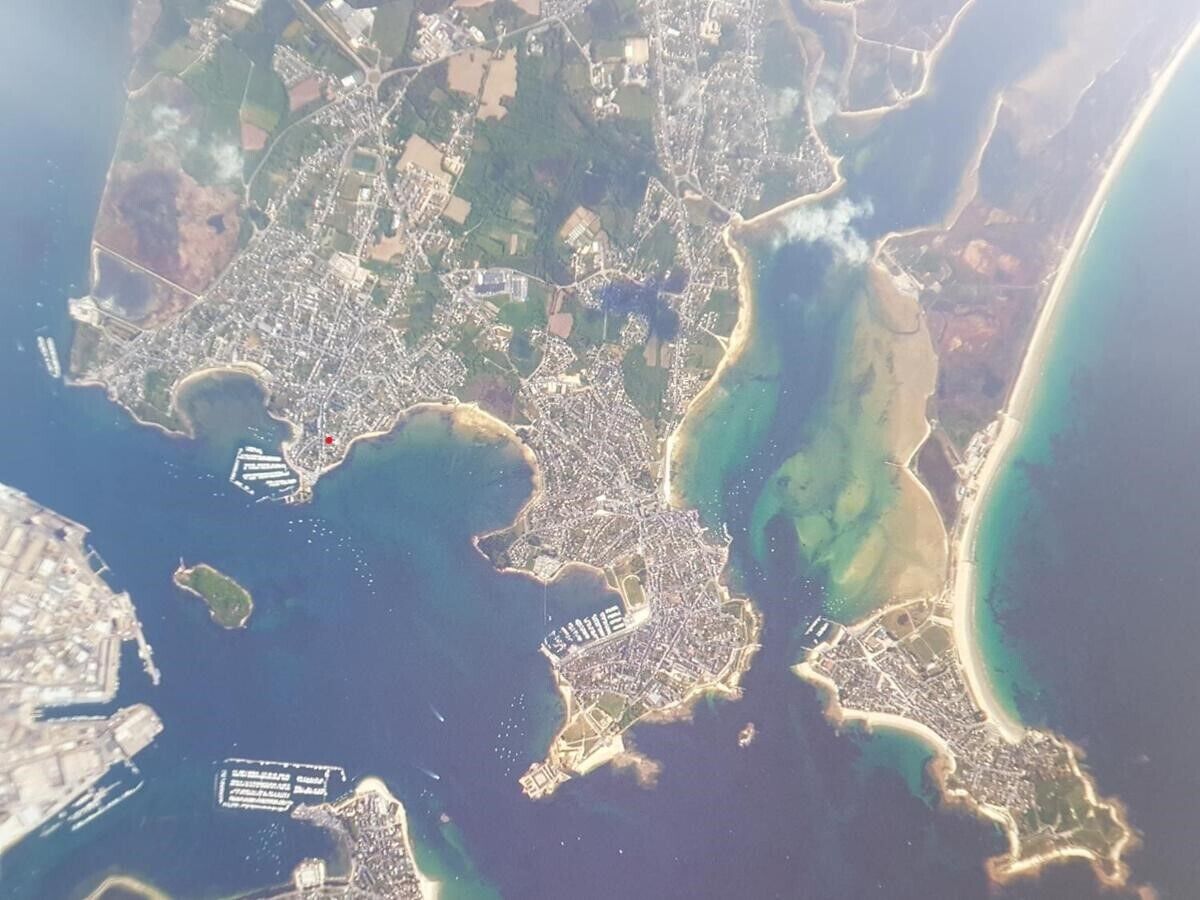 Una vista aerea di una città costiera con una zona urbana densa, un’ampia marina e una spiaggia.