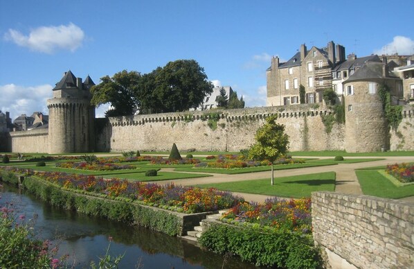 A historic castle with a moat, formal gardens, and a large stone wall.