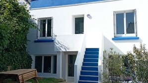 A two-story house with a blue roof and white walls, a front door, and a set of stairs leading to the entrance. - LE Kevav - A 300 M DE LA Cote (Locmiquélic)