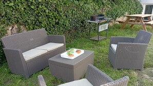 A patio area with wicker furniture, including a sofa and chairs, a small table with a tray of food, and a grill. - LE Kevav - A 300 M DE LA Cote (Locmiquélic)