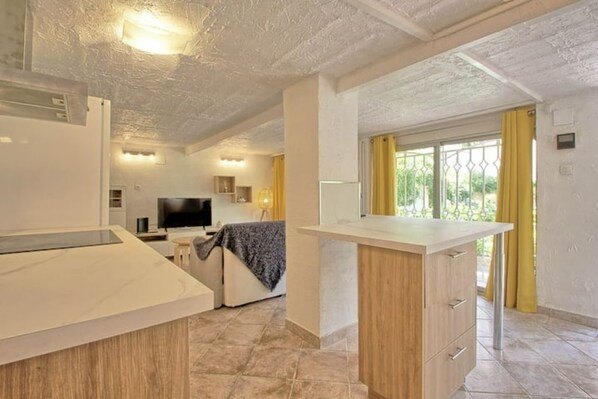 Una cocina moderna con una isla central, un área de comedor con un sofá y vistas al exterior a través de una ventana con cortinas amarillas.