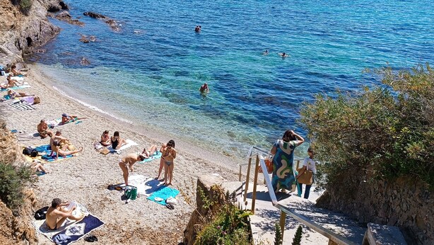 Une plage où l’on peut se prélasser au soleil et se baigner, avec une eau d’un bleu limpide et un paysage rocheux.