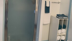 A bathroom with a glass shower door, a towel rack with folded towels, and a storage unit with towels. - Near The Lake (Bee Branch)