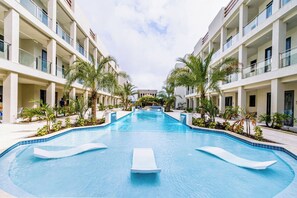 Una piscina con lettini, circondata da palme e edifici moderni.