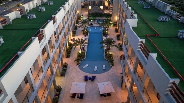 A hotel courtyard with a swimming pool, lounge chairs, and a central water feature.