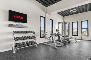 A gym with weightlifting equipment, dumbbells, and a TV displaying the Netflix logo.
