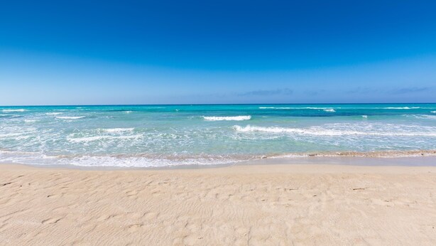 Une plage avec une eau d’un bleu limpide et un rivage sablonneux.