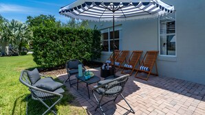 Une terrasse avec des meubles d’extérieur, un parasol à rayures et une haie.