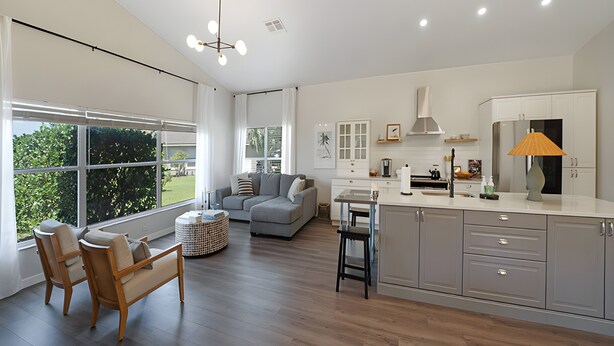 Une cuisine moderne dotée d’un îlot central, un coin repas avec une table et des chaises, et un salon avec un canapé et une table basse.