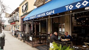 Ein Außenbereich des George's Greek Cafe mit blauem Markisenvorzelt und Tischen.