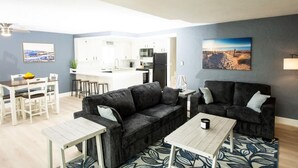 Ein modernes Wohnzimmer mit einem schwarzen Sofa, einem Holztisch und einem Essbereich mit weißen Stühlen und einer kleinen Kücheninsel.