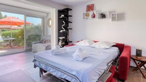 Une chambre d’hôtel moderne avec un lit, un canapé rouge, une petite table et un balcon équipé d’un parasol.