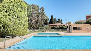 Une piscine dotée d’une terrasse carrelée, entourée d’une clôture et de verdure.
