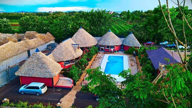 Un complexe hôtelier doté de bungalows aux toits de chaume, d’une piscine et d’un bâtiment rouge.